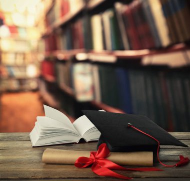 Mezuniyet şapkası, kitap ve diploması kütüphanedeki ahşap masada.