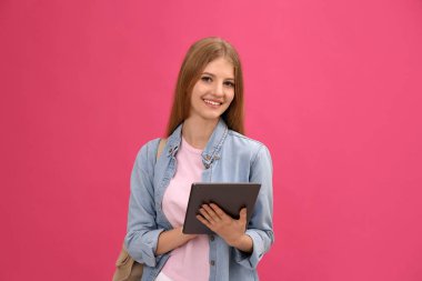 Pembe arka planda tablet ve sırt çantası olan genç bir öğrenci.