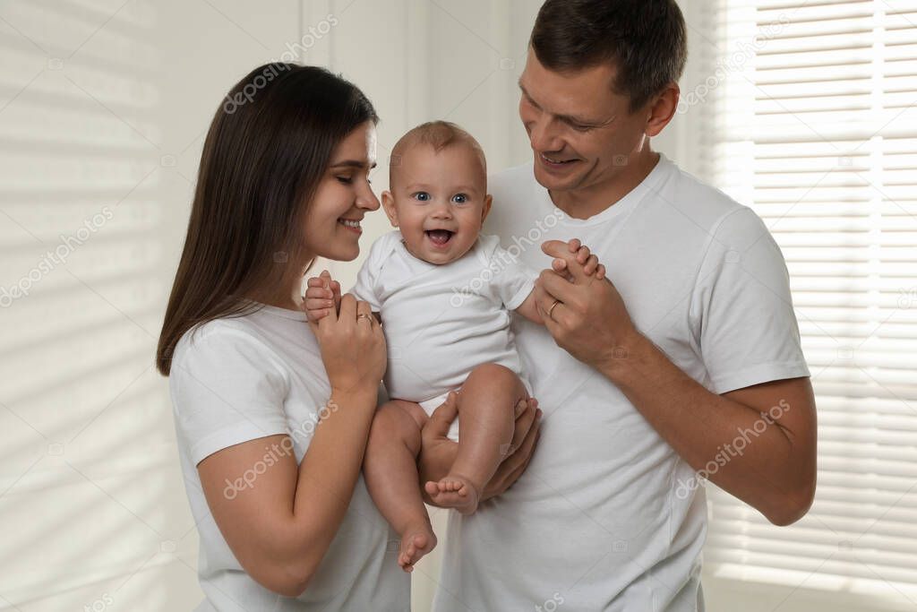 Happy family. Couple with their cute baby near window indoors