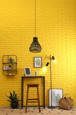 Tabletli ve tabletli yüksek ahşap masa sarı tuğla duvarın yanında ayakta duruyor. Şık iç mekan