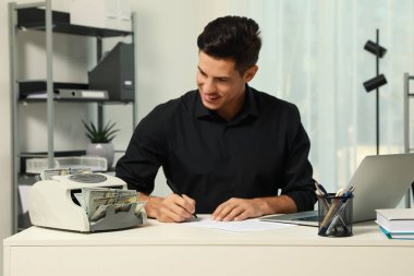 Beyaz masada banknot tezgahı kullanan bir adam.