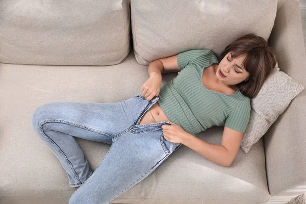 Young Woman Struggling Squeeze Tight Jeans While Lying Sofa View — Stock Photo, Image
