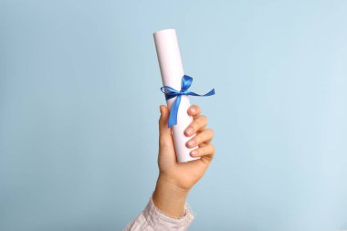 Açık mavi arka planda kurdeleli öğrenci diploması, yakın plan.