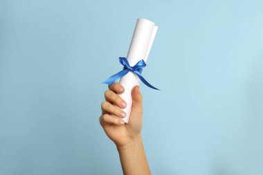 Açık mavi arka planda kurdeleli öğrenci diploması, yakın plan.