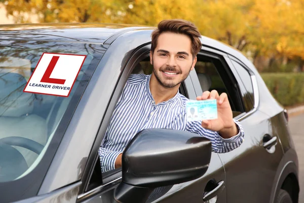 Young man holding driving license in car