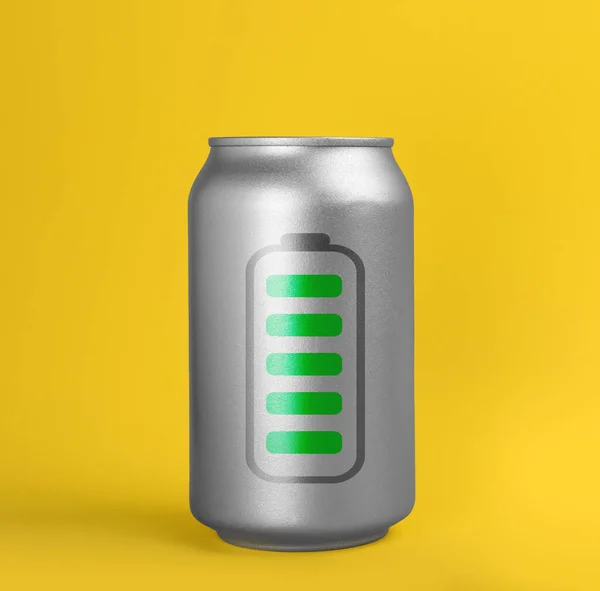 黄色の背景に完全に充電されたバッテリーの写真とエネルギードリンクの缶 — ストック写真