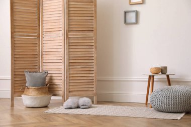 Katlanan ekran, küçük masa ve beyaz duvarın yanında örülmüş puf. İç tasarım