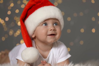 Tüylü halıda bulanık ışıklara karşı Noel Baba şapkalı şirin bebek. Noel kutlaması