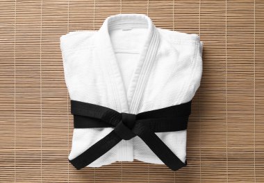 Martial arts uniform with black belt on bamboo mat, top view clipart