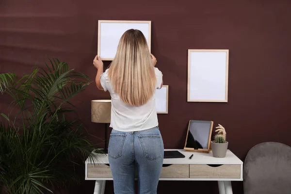 Vrouw Hangend Leeg Frame Aan Bruine Muur Binnenshuis Achteraanzicht Mockup — Stockfoto