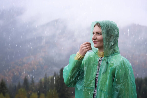 Young woman in raincoat enjoying mountain landscape under rain
