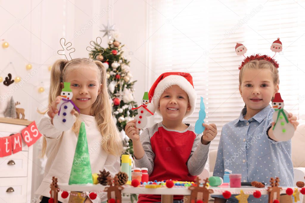 Cute little children with beautiful Christmas crafts at table decorated in room