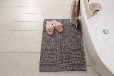 Banyodaki yumuşak gri banyo paspası ve terlikler.
