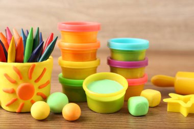 Aletlerle ve ahşap masada renkli kalemlerle oynanan parlak oyun hamuru seti.