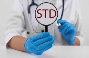 Doktor elinde büyüteç ve kısaltma STD ile beyaz masada, yakın plan.
