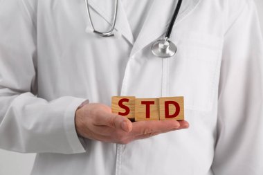 Doktor elinde tahta küplerle beyaz arka planda STD kısaltması tutuyor.