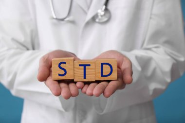 Doktor elinde tahta küplerle açık mavi arka planda STD kısaltması var.