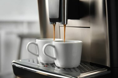 Espresso makinesi fincanlara kahve dolduruyor. Arka plan bulanık, yakın plan.