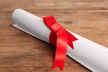 Ahşap masada kırmızı kurdeleli öğrenci diploması, yakın plan.