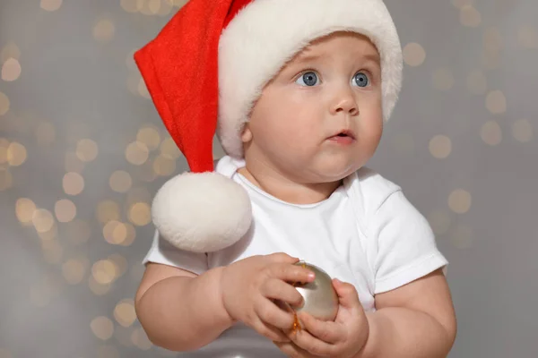 Leuke Baby Santa Hoed Met Kerstbal Tegen Wazig Licht — Stockfoto