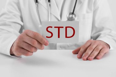 Beyaz masada kısaltması STD olan kağıt tutucu doktor, yakın plan.