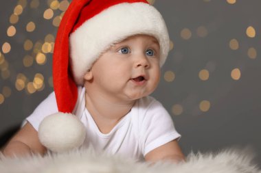 Tüylü halıda bulanık ışıklara karşı Noel Baba şapkalı şirin bebek. Noel kutlaması