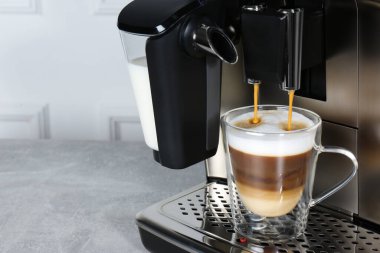 Modern kahve makinesi, yakın plan gri masada cam fincana latte yapıyor. Metin için boşluk