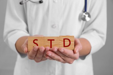 Doktor elinde tahta küplerle Gri arka planda STD kısaltması, yakın plan