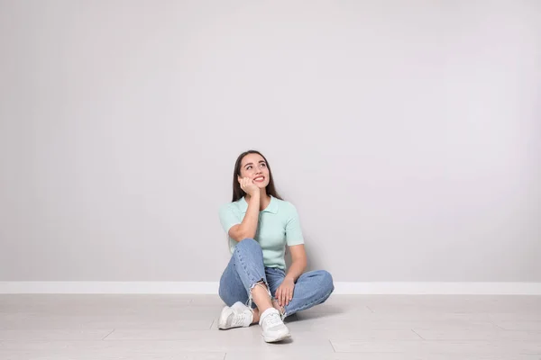 Jonge Vrouw Zit Vloer Buurt Van Lichtgrijze Muur Binnen — Stockfoto