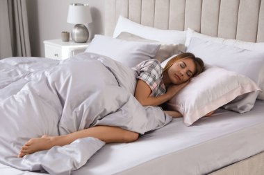 Güzel bir kadın, ipek çarşaflarla rahat bir yatakta uyuyor.