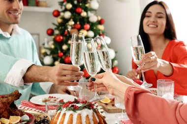 Mutlu arkadaşlar şenlikli akşam yemeğinde köpüklü şarap kadehlerini tokuştururlar. Noel arifesi