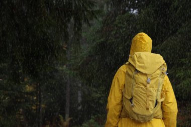 Yağmurluklu ve sırt çantalı bir kadın yağmur altında, arka planda