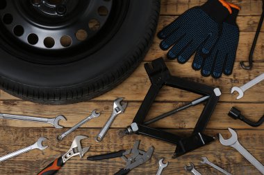 Araba tekerleği, makas kriko, eldivenler ve tahta yüzeyde farklı aletler, düz yatış