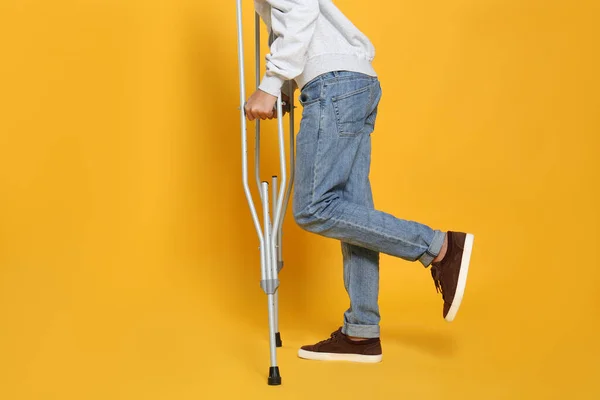黄色の背景に松葉杖を使って足を負傷した男を閉じます — ストック写真