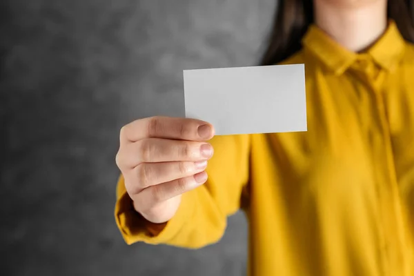 Woman holding blank business card on grey background, closeup. Mockup for design