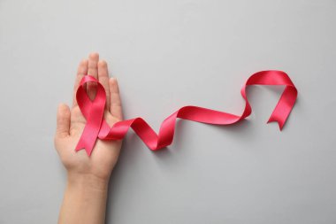 Açık gri arka planda pembe kurdeleli bir kadın, üst manzara. Göğüs kanseri farkındalığı konsepti