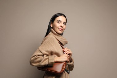 Bej arka planda şık bir çantası olan şık bir genç kadın.