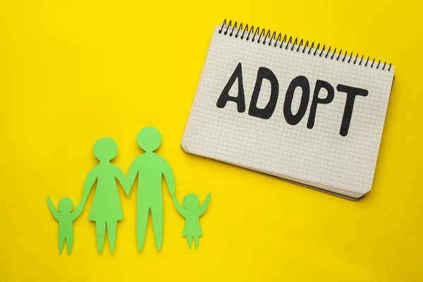 Familienfigur Und Notizbuch Mit Wort Adopt Auf Gelbem Hintergrund Flache — Stockfoto