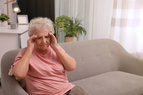 一位头痛的老妇人坐在家里的沙发上 案文的篇幅 — 图库照片