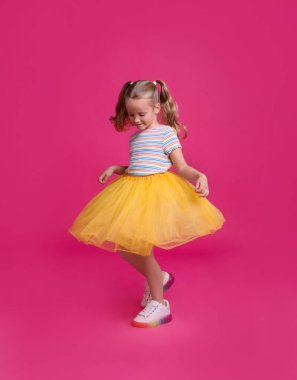Tutu etekli şirin kız pembe arka planda dans ediyor.