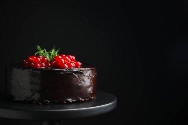 Tatlı standında böğürtlenli ve biberiyeli ev yapımı çikolatalı kek, siyah arka planda. Metin için boşluk