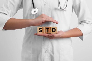Doktor elinde tahta küplerle beyaz arka planda STD kısaltması tutuyor.
