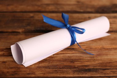 Ahşap masada mavi kurdeleli bir öğrenci diploması.