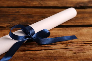 Ahşap masada mavi kurdeleli öğrenci diploması, yakın plan.