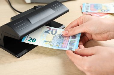 Bir kadın, ahşap masada Euro banknotunu detektörle kontrol ediyor. Yakın plan. Para inceleme aygıtı