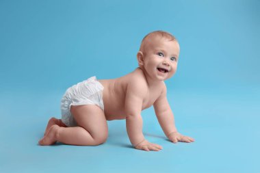 Kuru, yumuşak bezli, açık mavi arka planda emekleyen şirin bir bebek.
