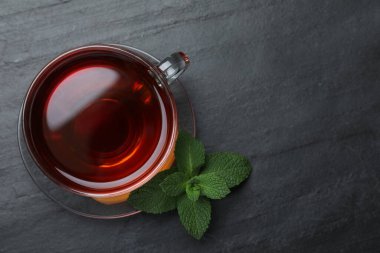 Bir fincan sıcak aromatik çay, siyah masada nane şekeri, düz uzanmış. Metin için boşluk