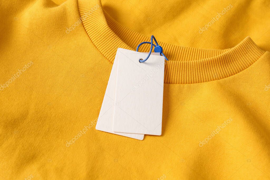Blank white tags on yellow sweatshirt, top view. Space for text