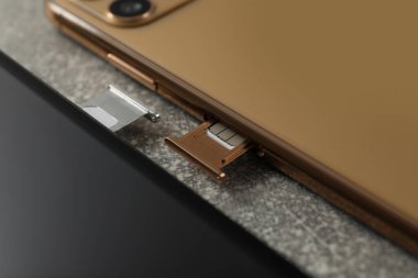 Gri masadaki tepsilerde Sim kartları olan cep telefonları, yakın plan.