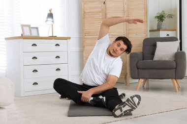 Evdeki paspasın üzerinde gerinen şişman bir adam.